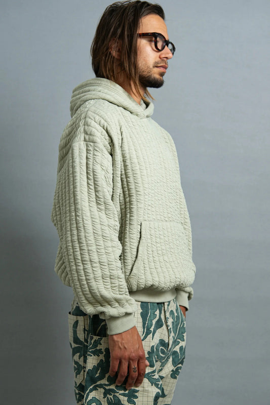 Man wearing a textured light green hoodie and patterned pants against a gray background