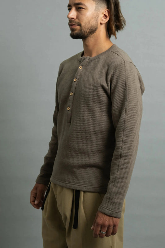 Profile of a man wearing a brown textured henley and beige pants