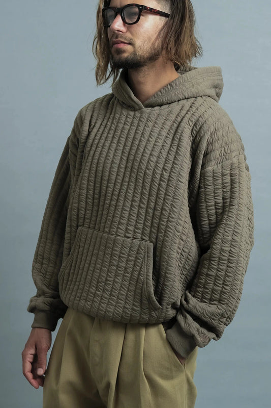 Man with long hair and glasses wearing a quilted brown hoodie and khaki pants