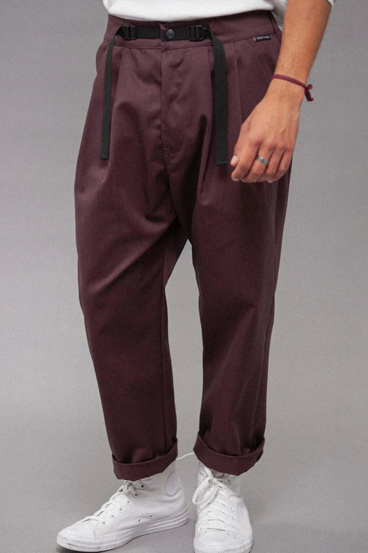 Close-up of a person wearing relaxed fit pleated burgundy pants with a black adjustable buckle belt, paired with white sneakers and a casual white top.