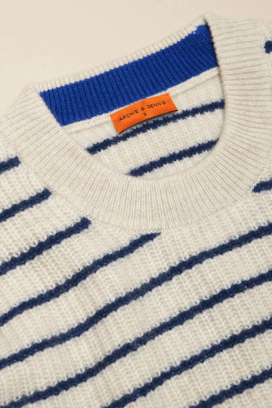 Close-up of a cream and navy striped sweater neckline with a ribbed collar and a bright orange brand label inside the collar.