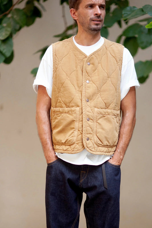 Man facing forward wearing a mustard quilted vest and blue jeans