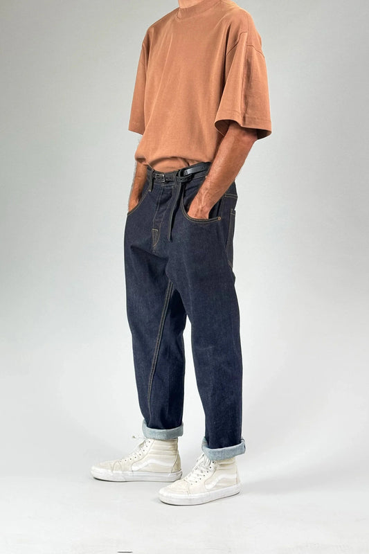 Model wearing blue selvedge denim pants and a brown t-shirt, hand in pockets