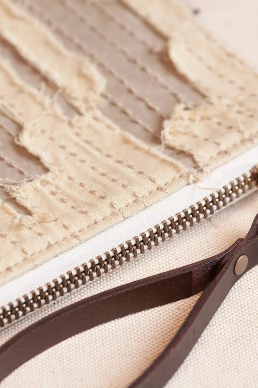 Close-up of a beige pouch with a gold zipper and brown leather strap