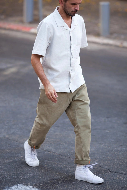 Man wearing an off-white bowling shirt and olive green pants, walking