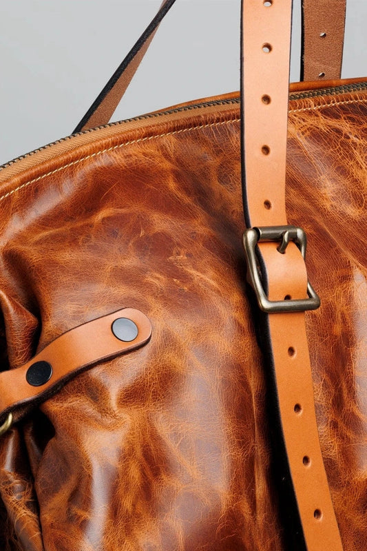 Close-up of a brown leather weekender bag with strap and buckle