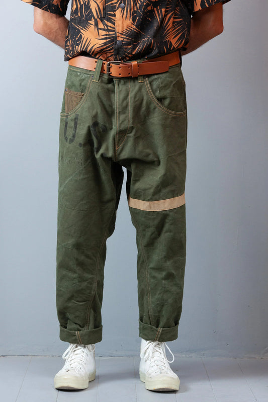 Man standing, wearing green carrot pants with a belt and white shoes