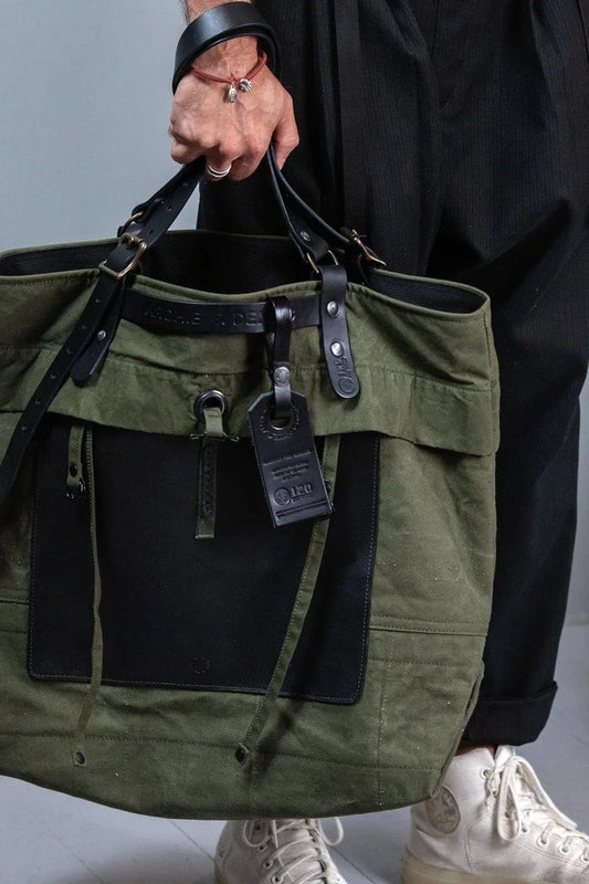 Person holding a green tote bag with black accents while wearing black pants