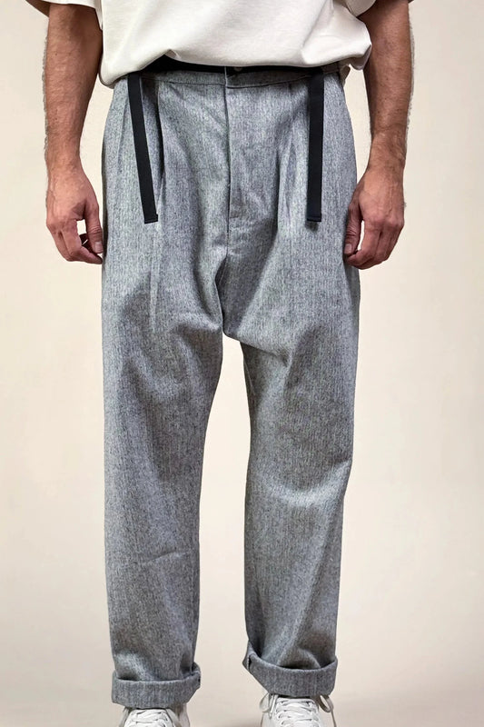 A person standing, wearing gray herringbone pants with black belt straps