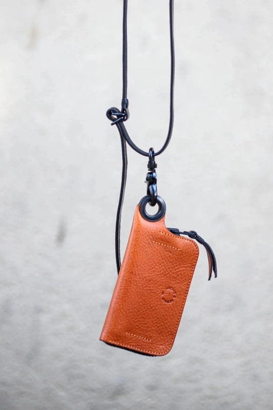 A brown leather keychain with a black strap hanging against a white background
