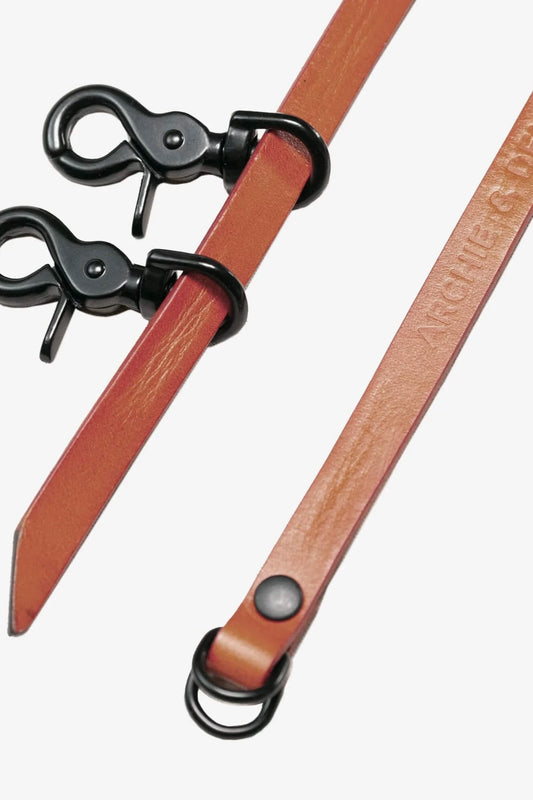 Brown leather strap with black metal clips and embossed branding detail, designed for use with holdall bags or similar accessories.