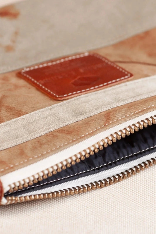Close-up of bronze pouch with zipper, brown accents, and light-colored fabric