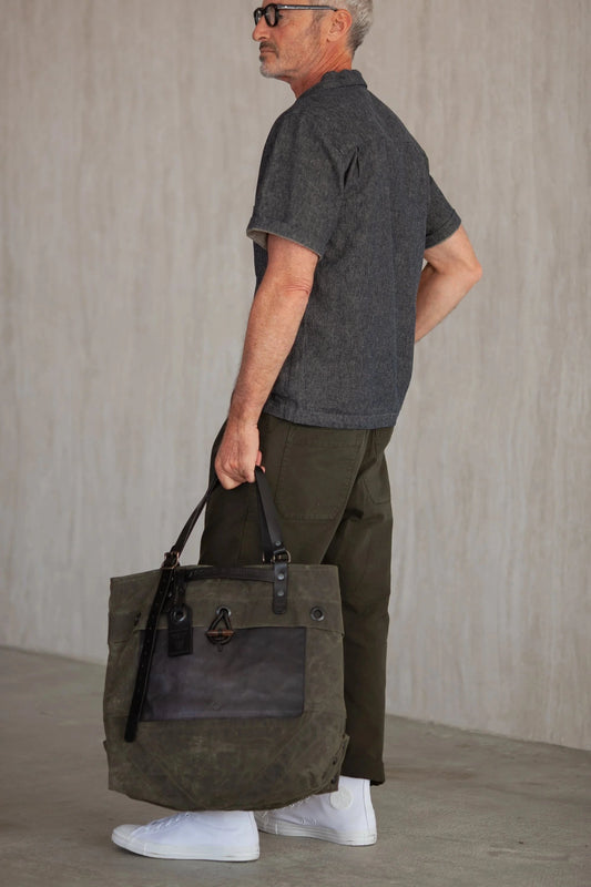 Man wearing a dark gray shirt and brown pants carrying a forest green tote
