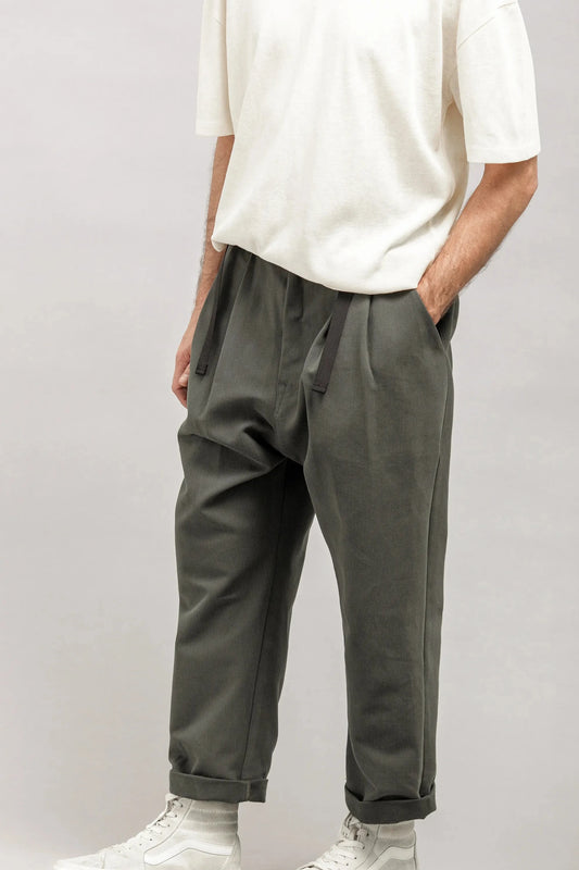 Man wearing relaxed fit pleated dark green pants with black drawstrings, paired with a loose white short-sleeve shirt and white high-top sneakers.