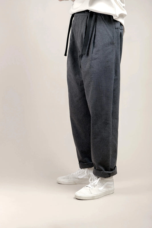 Side view of relaxed fit grey checkered pants with pleats, paired with white casual sneakers, featuring a comfortable drape and adjustable black waist ties.