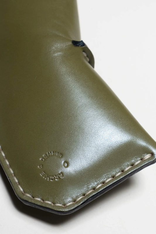 Close-up of a smooth olive green glasses case with neat stitching and subtle embossed branding on the leather surface, showcasing its quality craftsmanship.