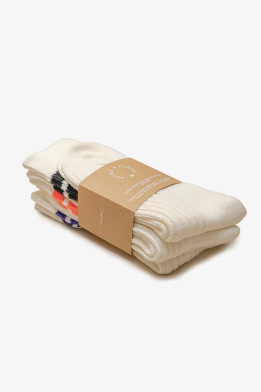 Three pairs of cream-colored socks neatly folded and stacked, each featuring a different colored double stripe near the cuff, wrapped with a brown paper band.
