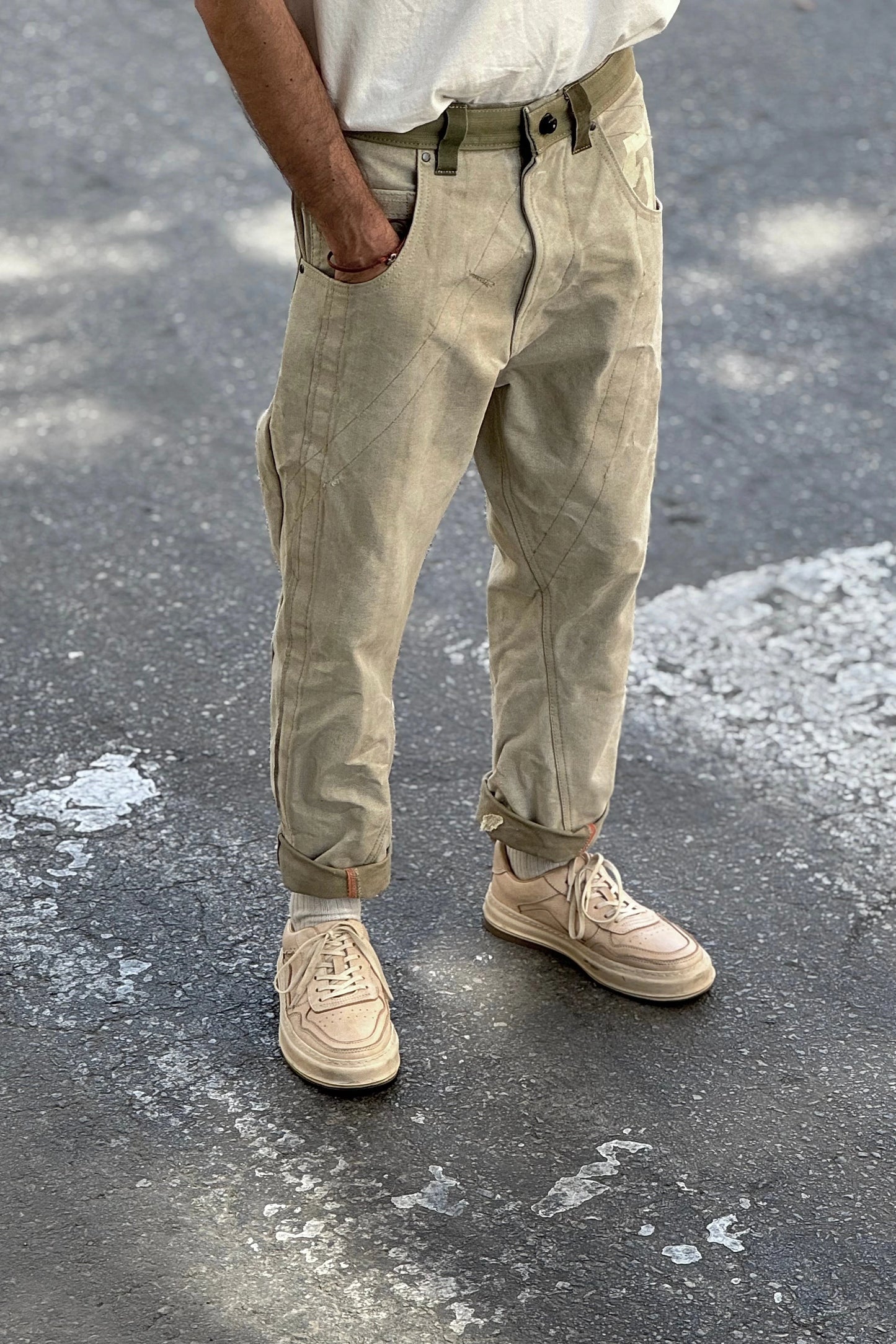 Person wearing beige pants and shoes standing on a textured pavement.
