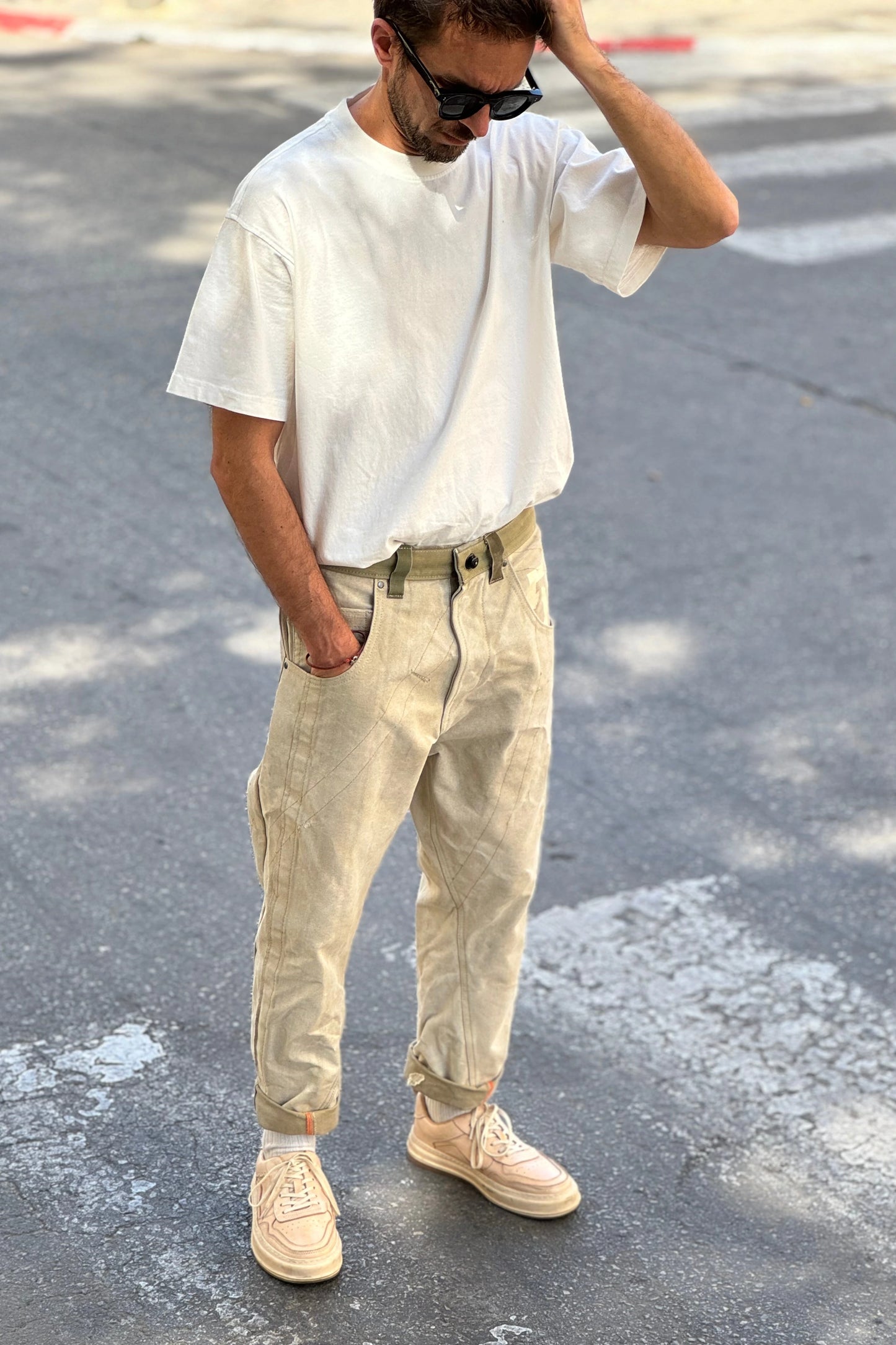 Man wearing a white t-shirt and beige pants standing on a street.