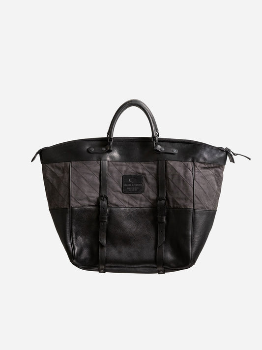 Black and dark gray handcrafted weekend bag with leather accents, dual buckle straps, and a sturdy handle, featuring a minimalist design ideal for utility-inspired menswear.