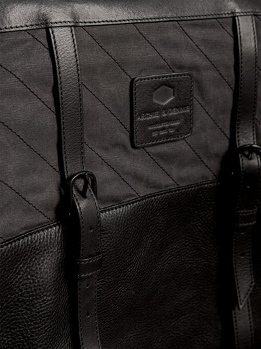 Close-up of a black handmade bag featuring textured leather, durable stitched fabric, adjustable leather straps, and a branded label, highlighting craftsmanship and utility style.