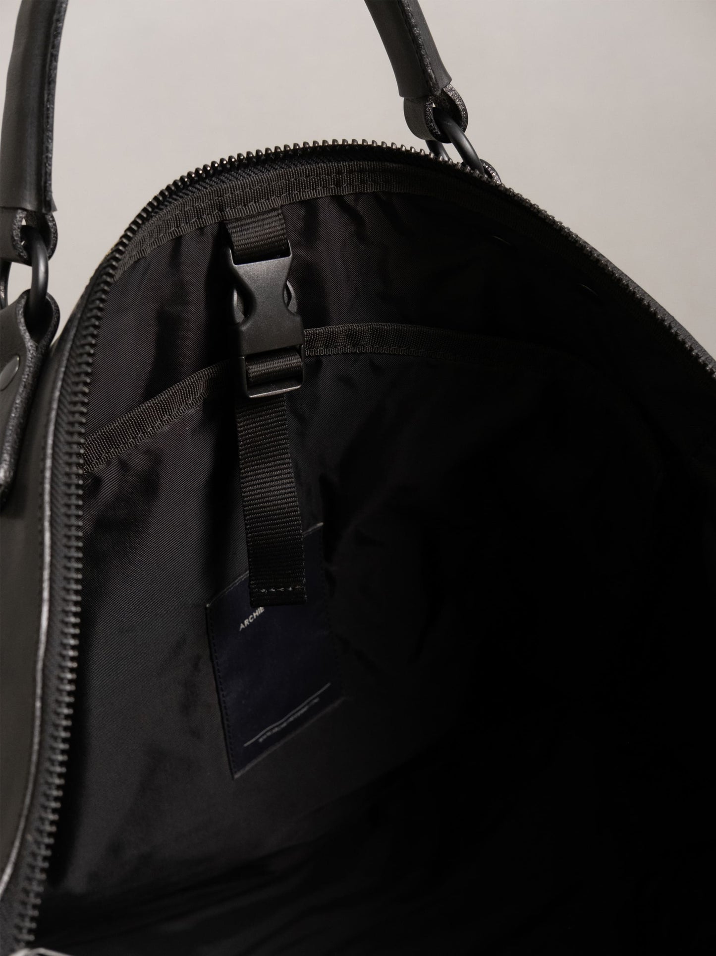Close-up view of the interior of a black handcrafted tote bag featuring a secure buckle strap and inner pocket, highlighting practical design and quality materials.
