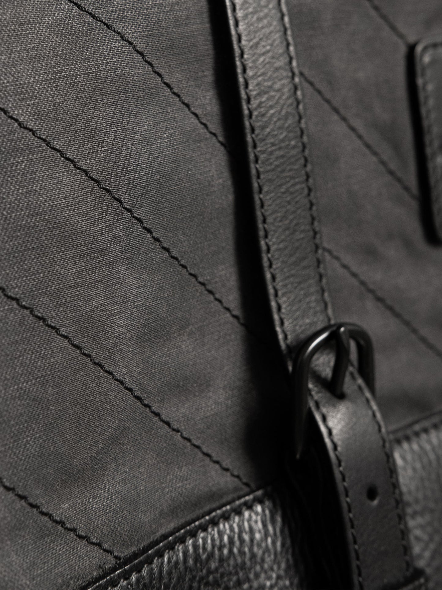Close-up of a black bag made with durable canvas and textured leather, featuring detailed stitching and a sleek adjustable strap buckle.