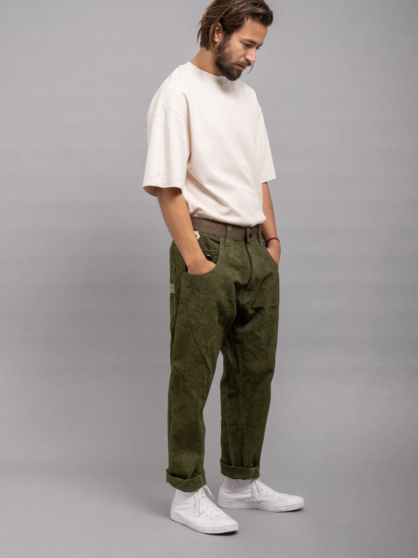 Man wearing a white shirt, green pants, and white sneakers on a gray background