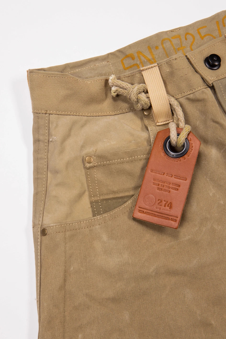 Close-up of beige army carrot pants with brown leather tag