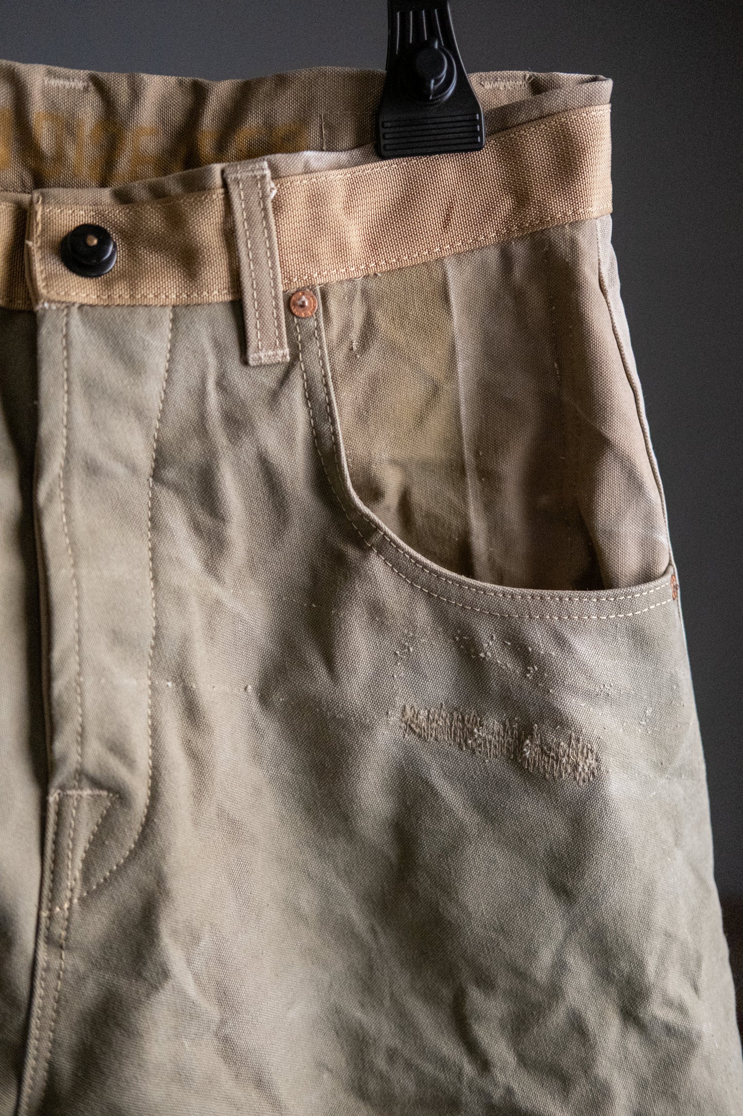 Close-up of a pair of beige pants with front pocket and button detail