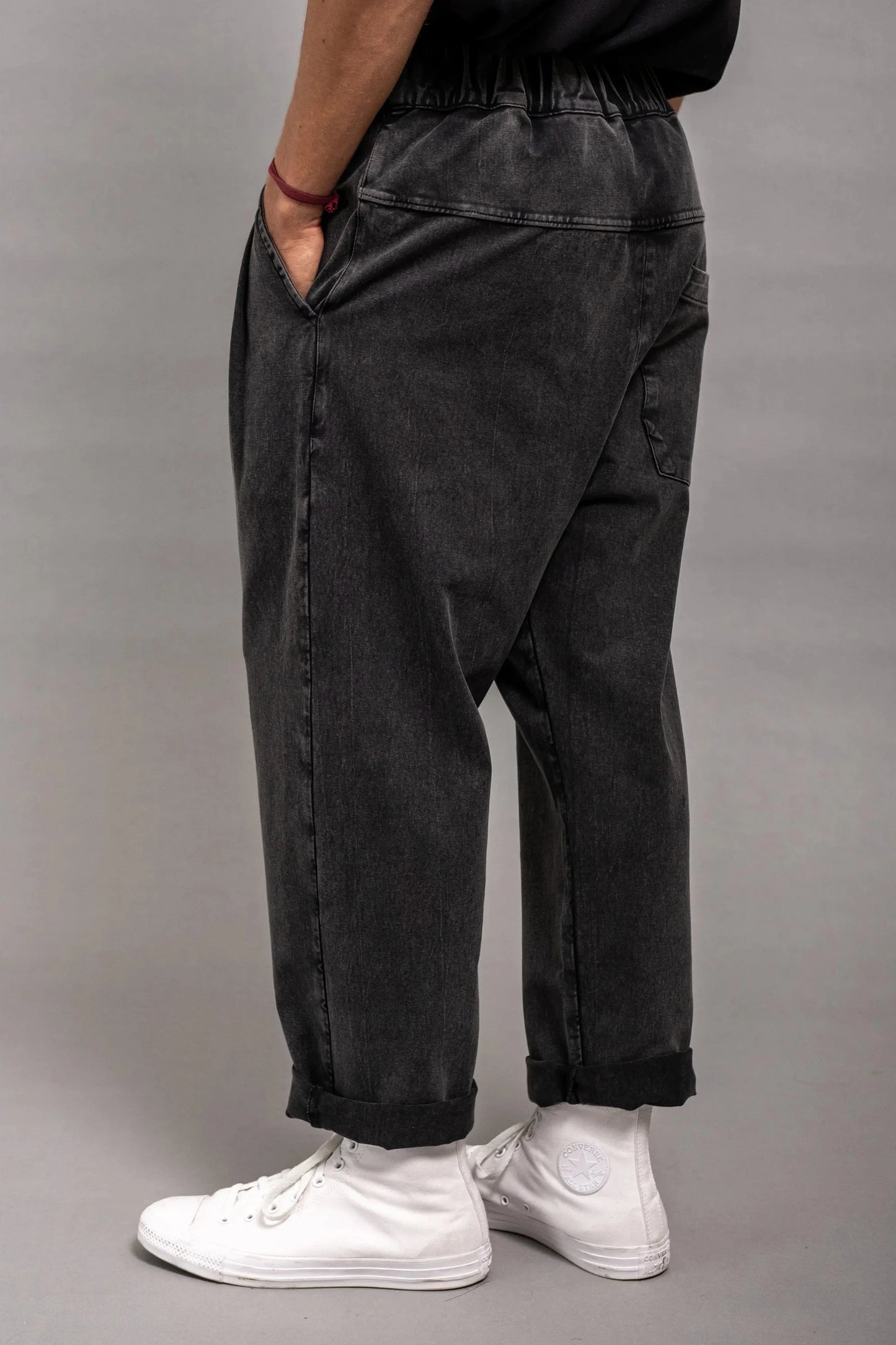 Side view of a person wearing relaxed fit black washed double-knit pants with an elastic waistband and cuffed hems, paired with white high-top sneakers.