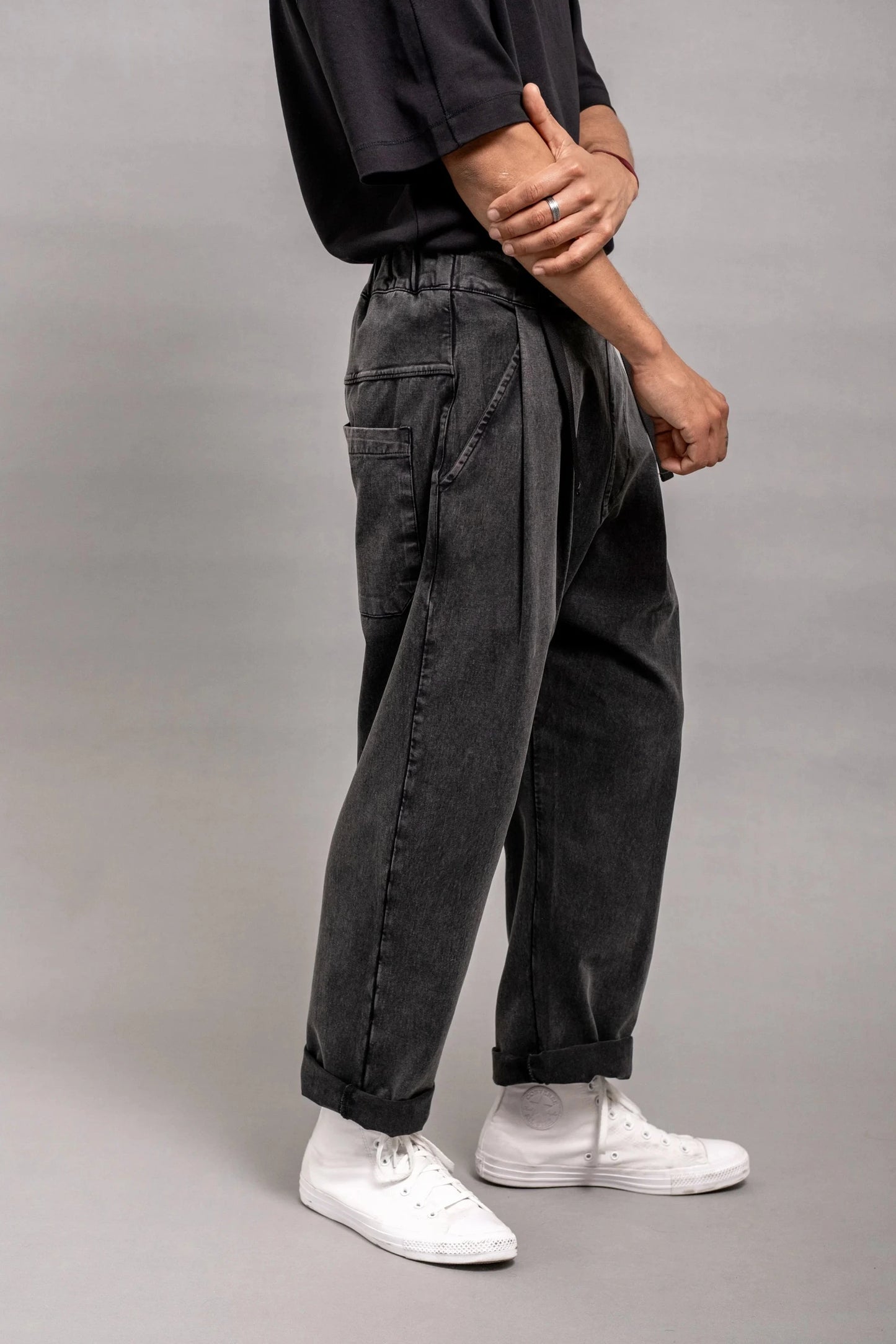 Side view of a person wearing relaxed fit pleated black wash double-knit pants paired with white high-top sneakers and a black short-sleeve shirt.