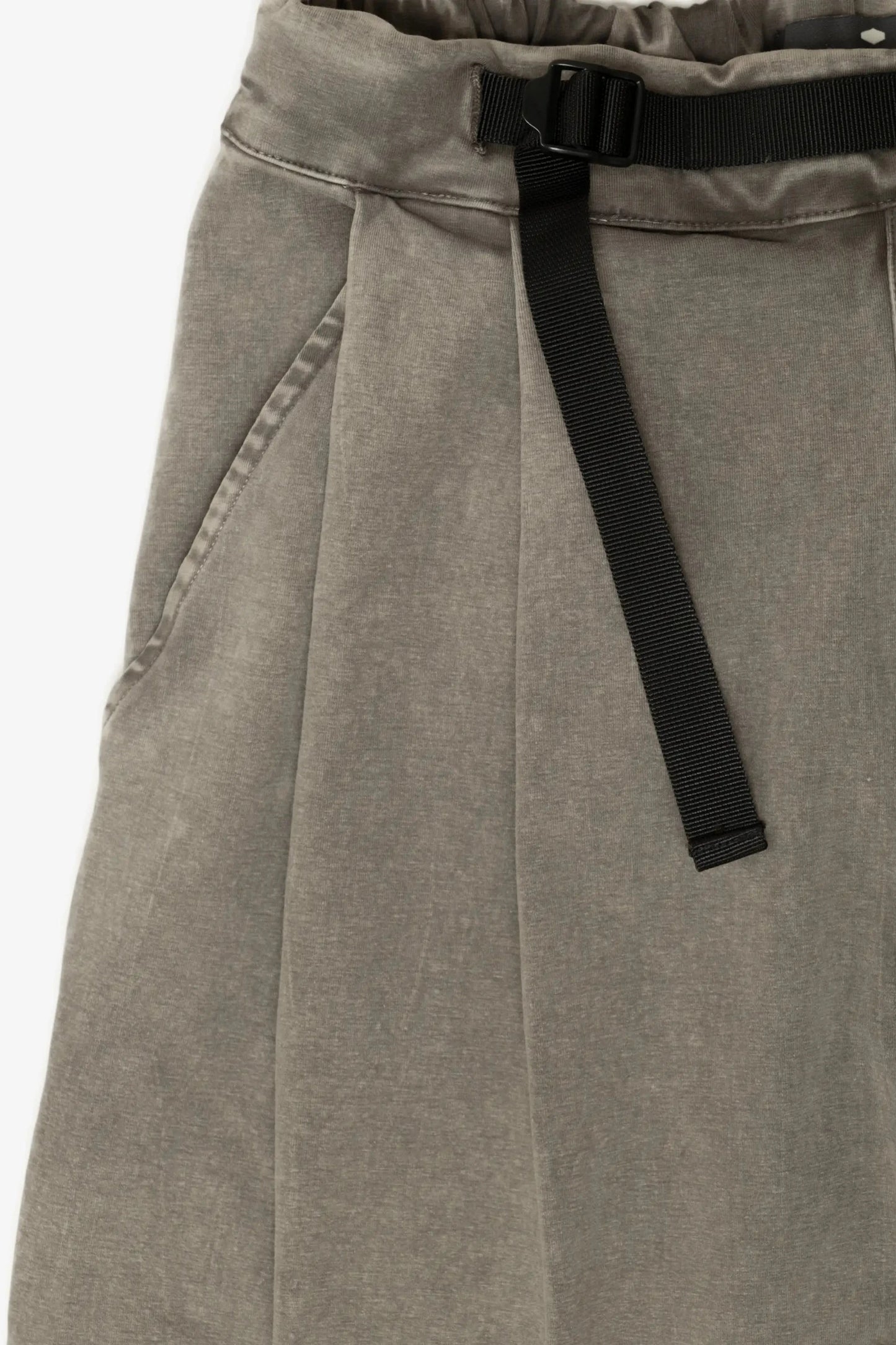 Close-up of relaxed fit pleated pants in washed earthy fabric with side pockets and an integrated black adjustable belt, highlighting military-inspired menswear details.