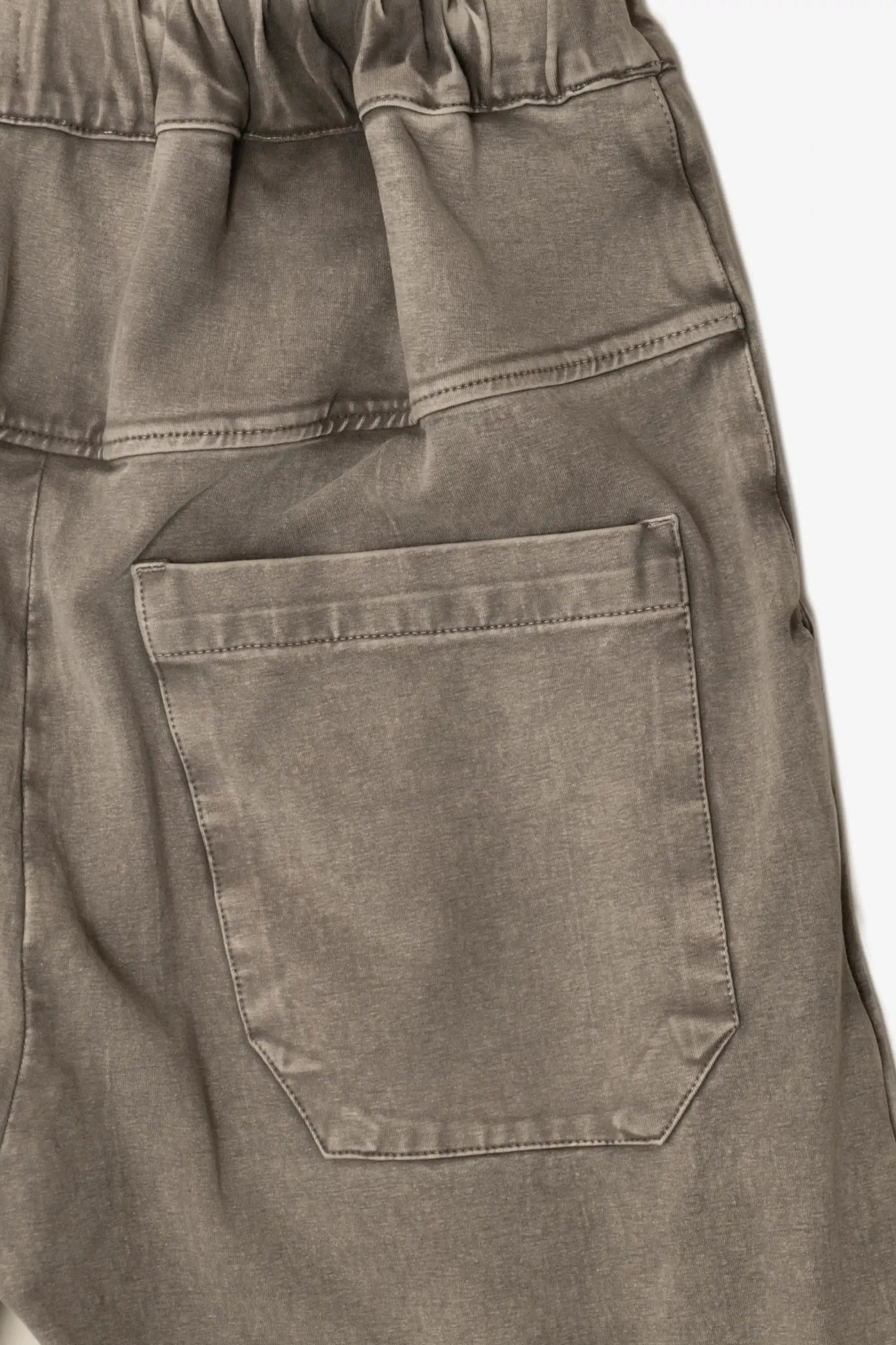 Close-up view of the back pocket on relaxed fit pants made from washed, double-knit fabric in a muted coffee color.