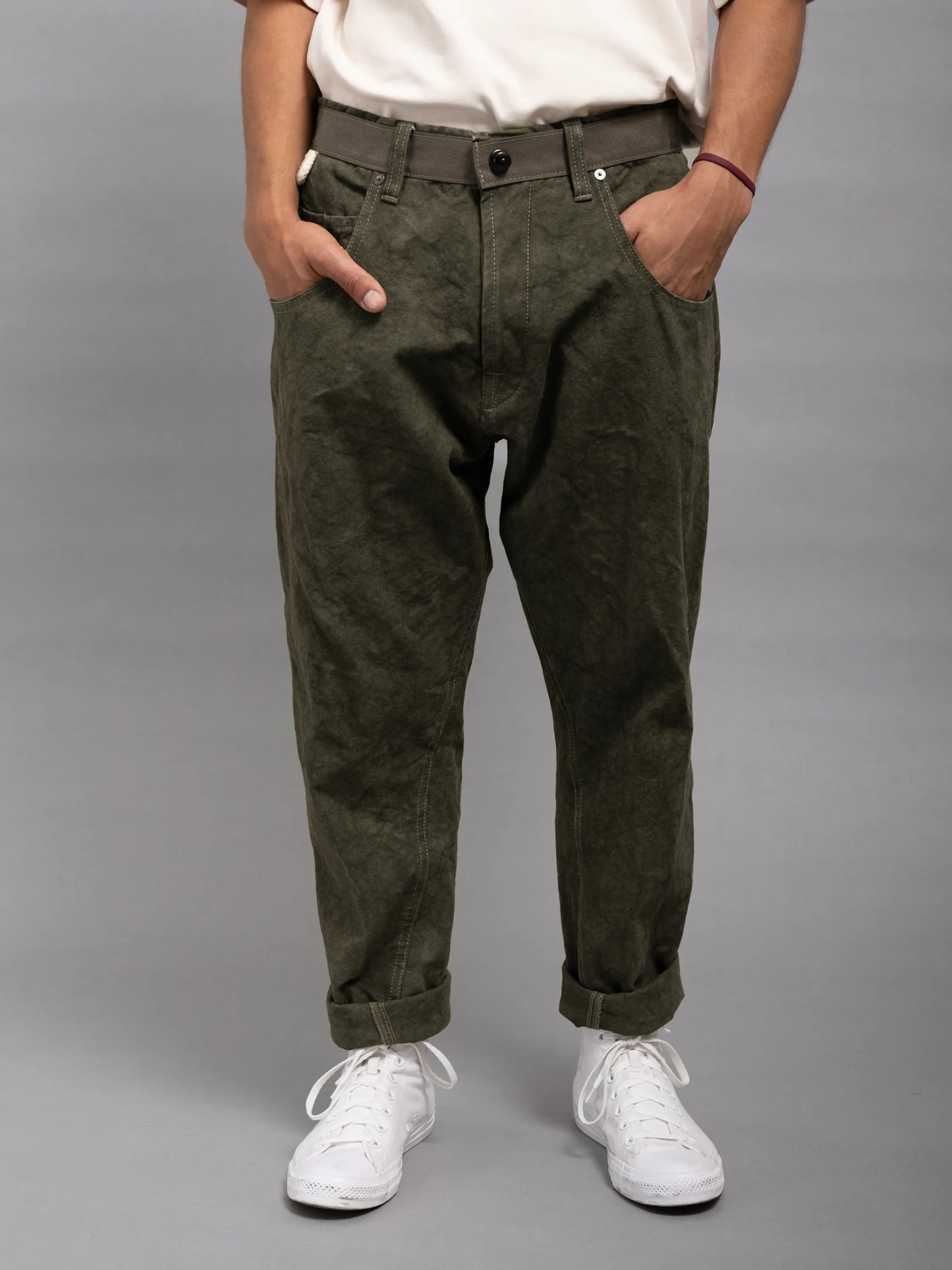 Front view of a person wearing olive green relaxed fit pants with rolled cuffs, paired with a white shirt and white sneakers, hands casually in pockets.