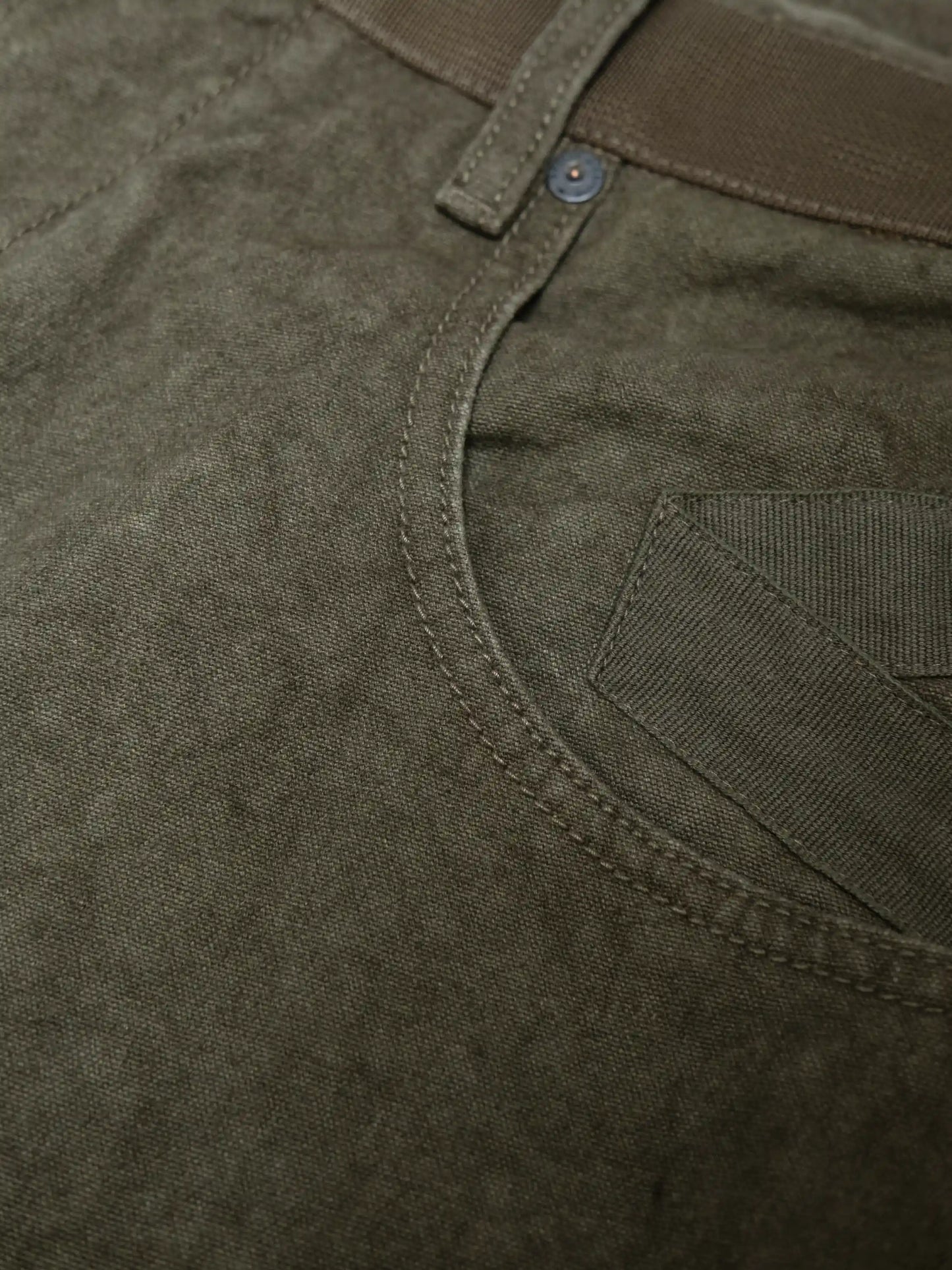 Close-up view of olive textured fabric with sturdy stitching and pocket detail on casual utility-style pants.