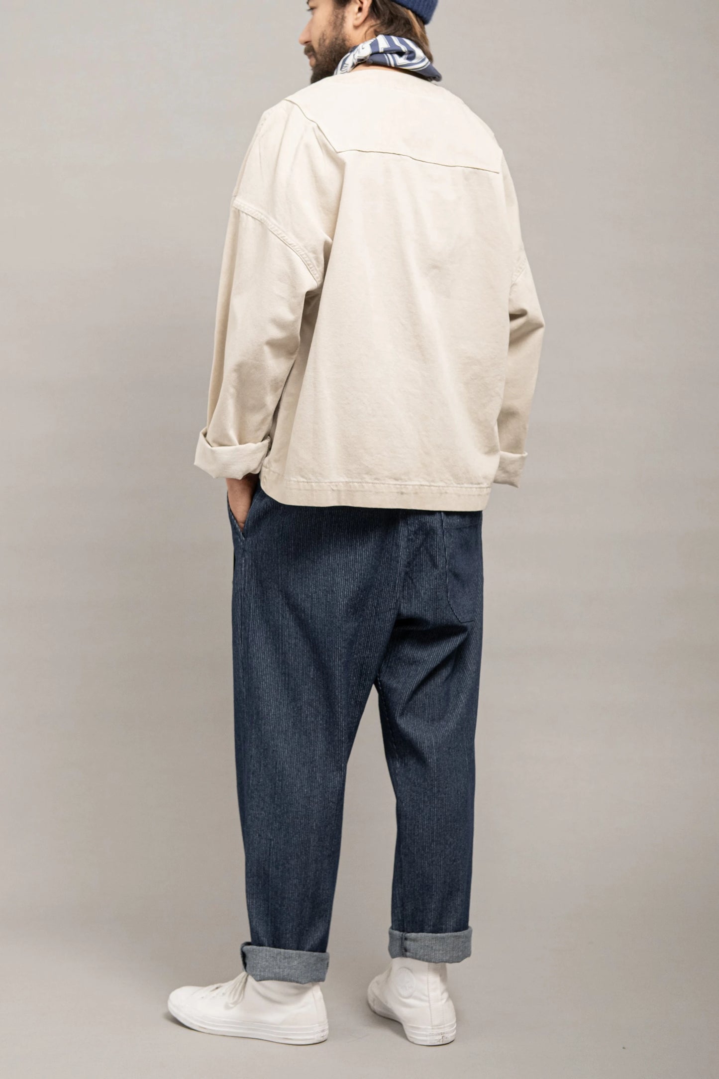 Man wearing relaxed fit indigo denim pants with cuffs, paired with a light beige jacket and white sneakers, showcasing a casual, utility-inspired menswear style.