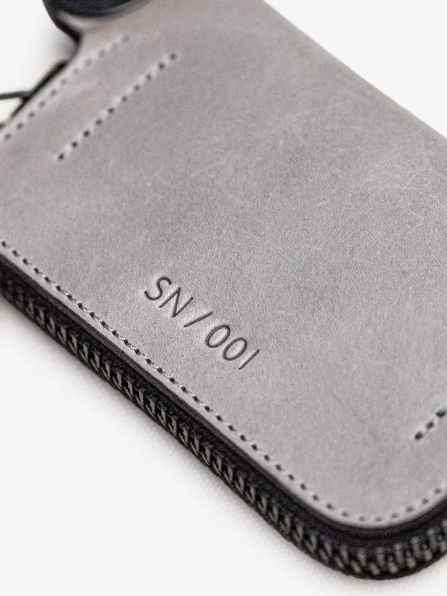 Close-up of a gray leather wallet corner with neat stitching and embossed serial number SN/001, showcasing minimalist craftsmanship and utility-inspired design.