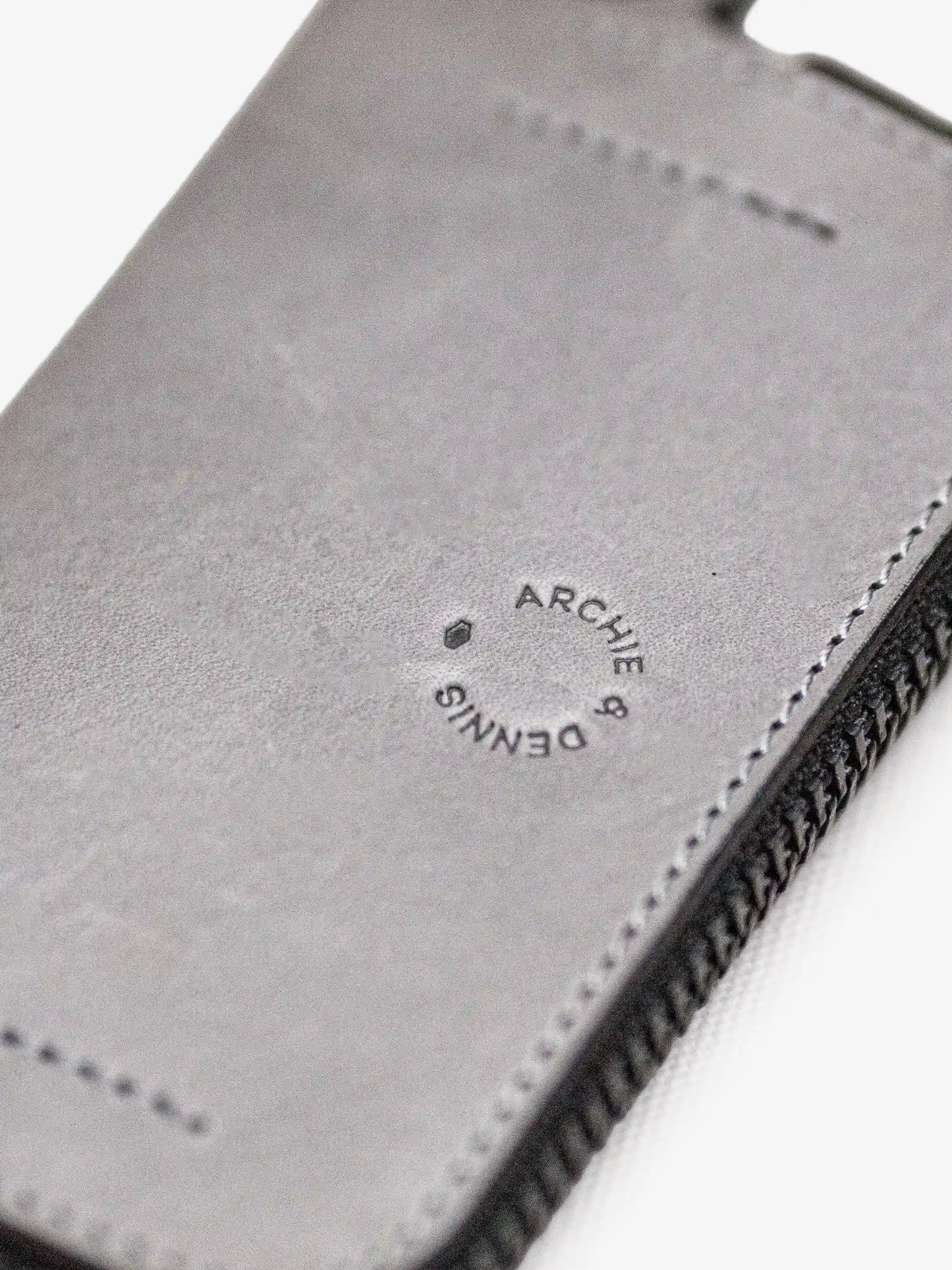 Close-up of a gray leather wallet featuring detailed stitching and a subtle embossed logo from Archie & Dennis, showcasing minimalist craftsmanship and quality material.