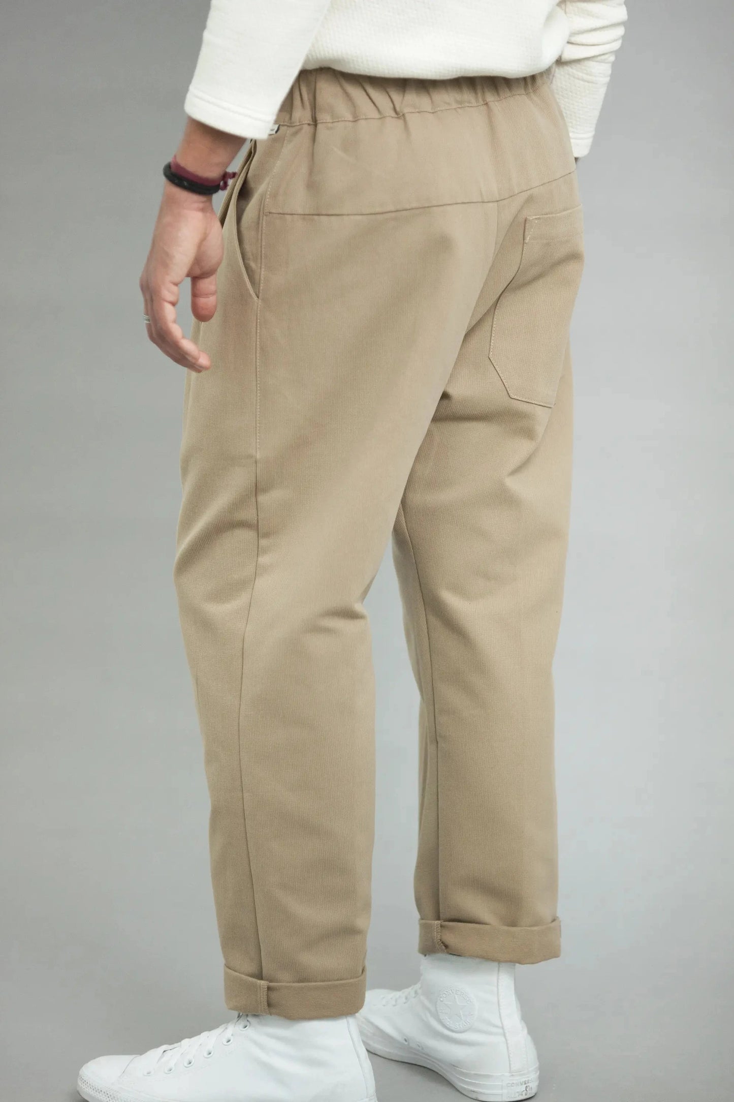 Back view of beige relaxed fit men’s pants with elastic waistband and single back pocket, styled with white sneakers and a casual white long sleeve top.