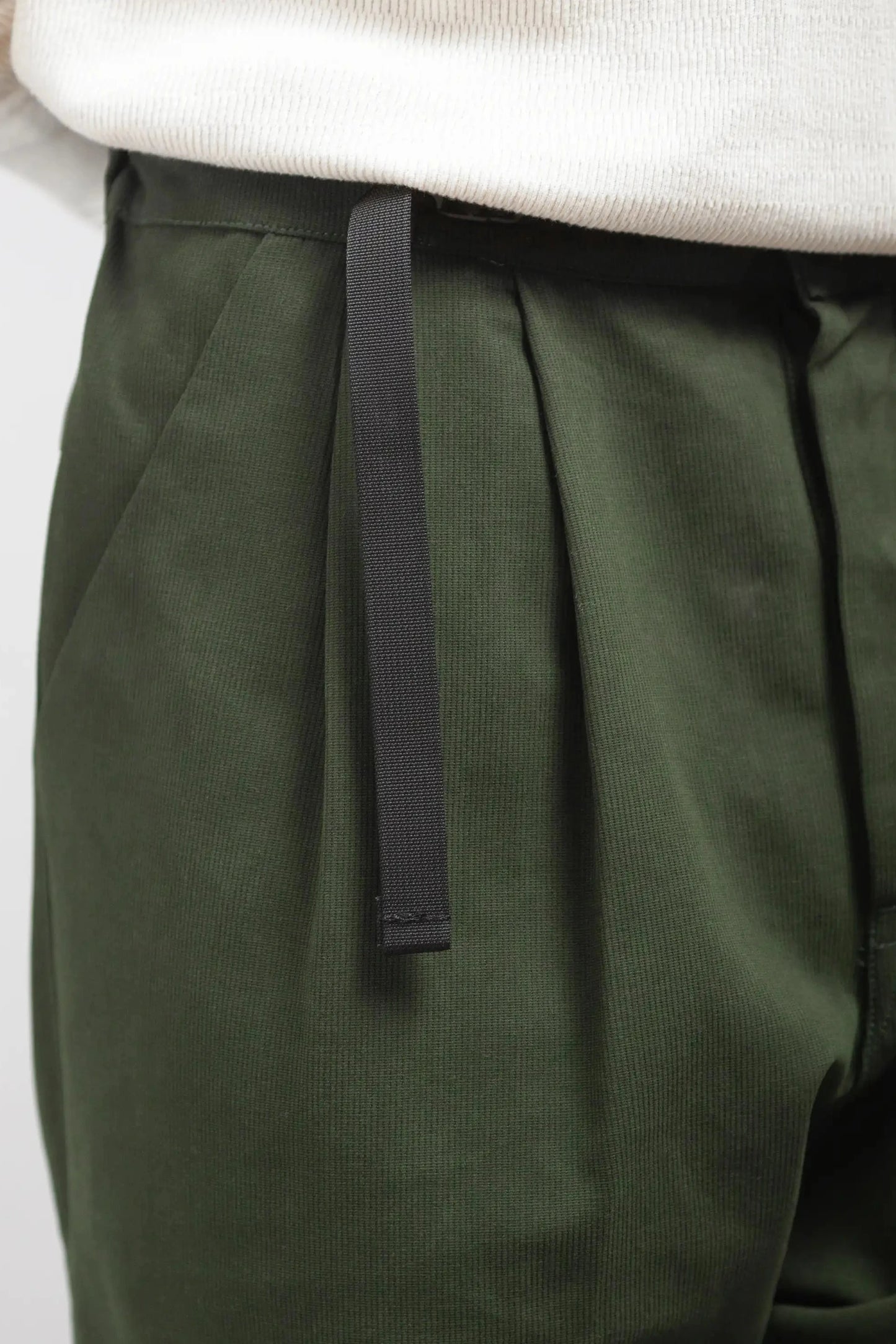 Close-up of dark green pleated pants with a relaxed fit and a black adjustable drawstring, styled with a white textured top.
