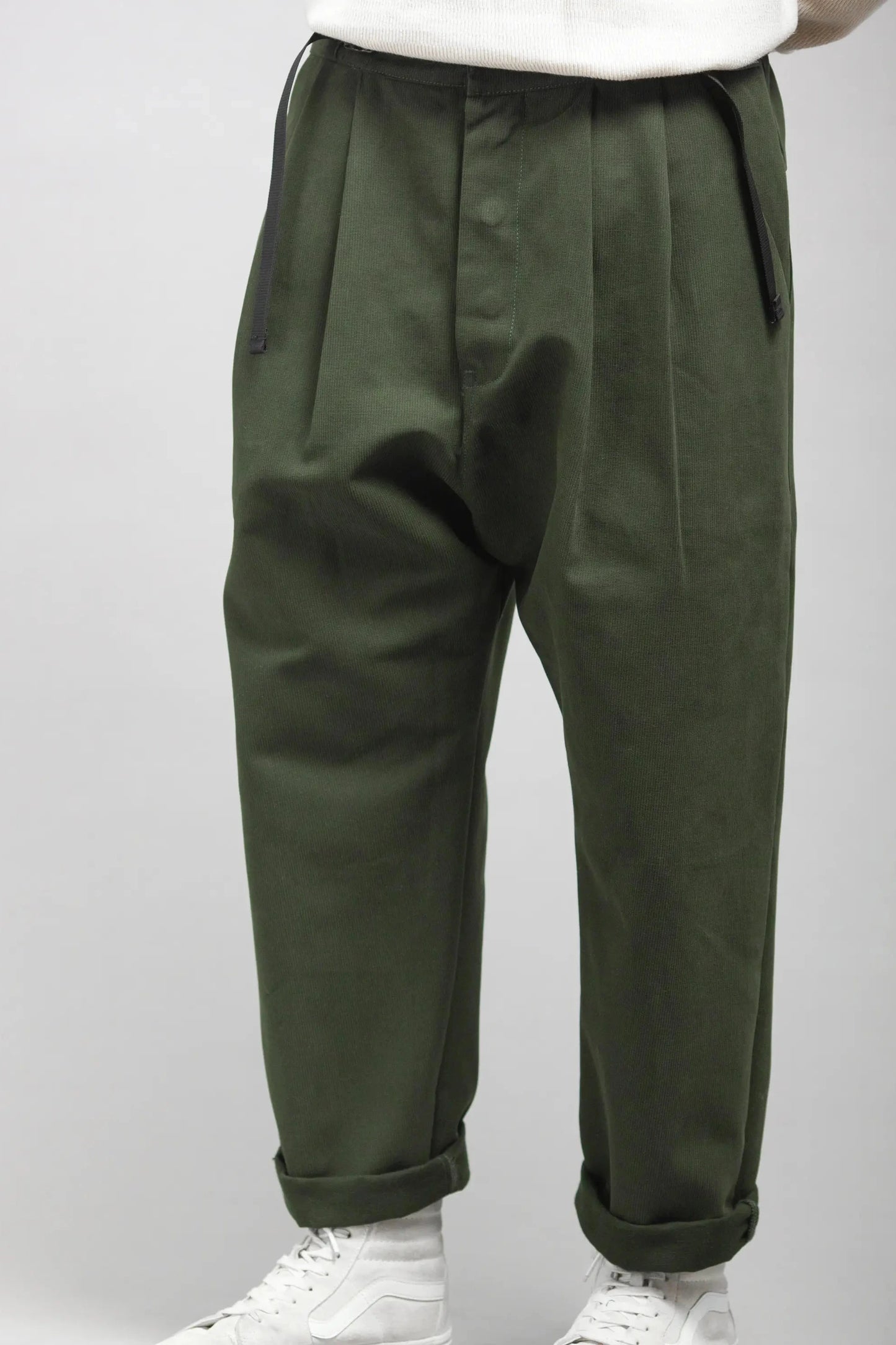 Relaxed fit pleated men's pants in a deep bottle green shade with cuffed hems, styled with casual white sneakers for a contemporary look.