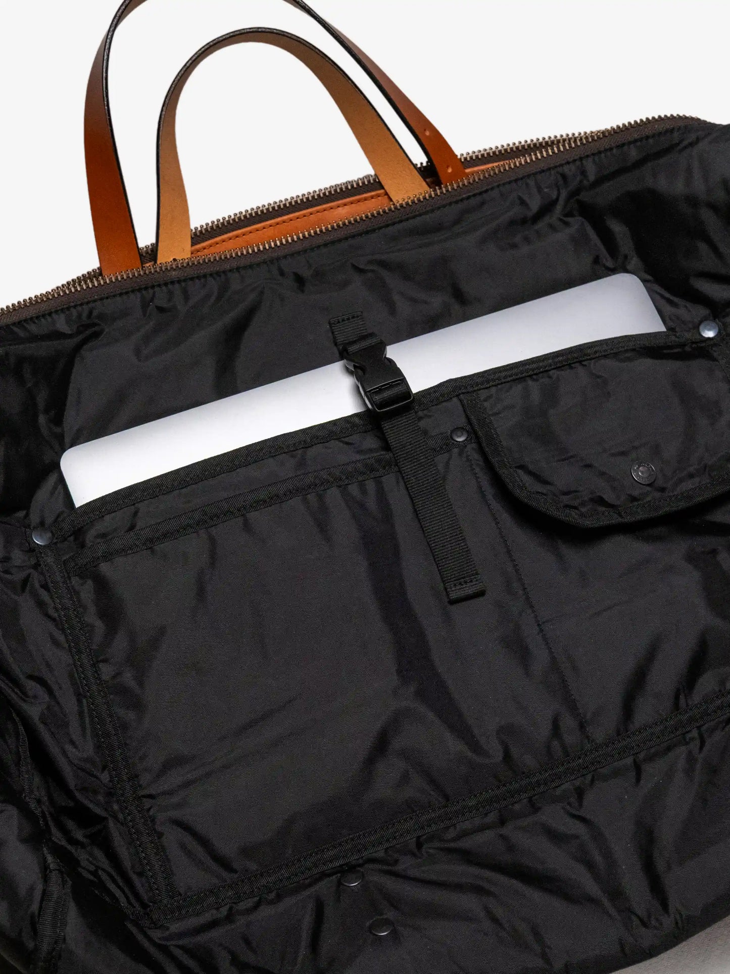 Interior view of a black weekend bag with leather handles, featuring a secure padded laptop compartment and multiple utility pockets for organizing essentials.