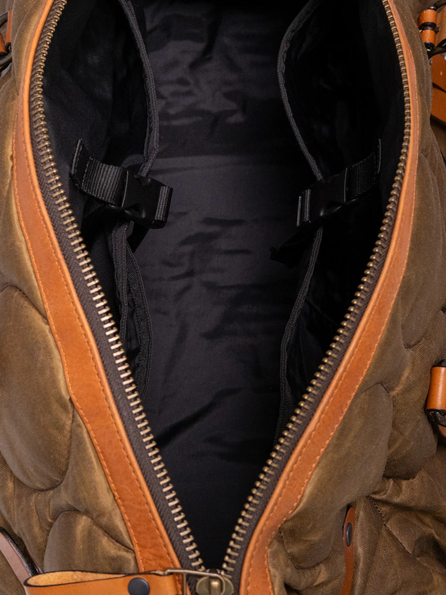 Top view of an open quilted weekend bag with black interior lining, adjustable straps inside, and a sturdy brass zipper framed by brown leather trim