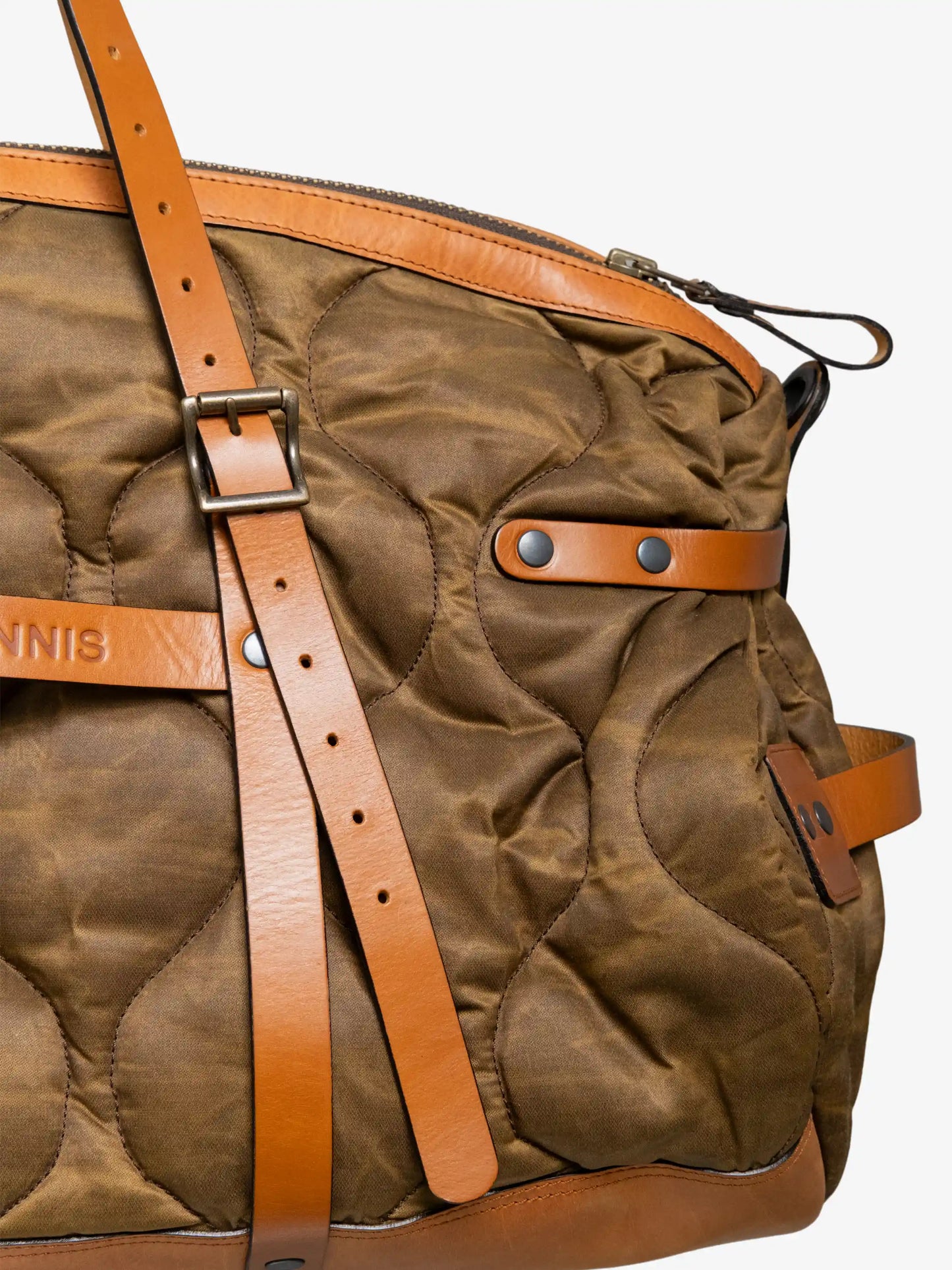 Close-up of a quilted olive green weekend bag with tan leather straps, buckles, and rivet details in a utility-inspired style.