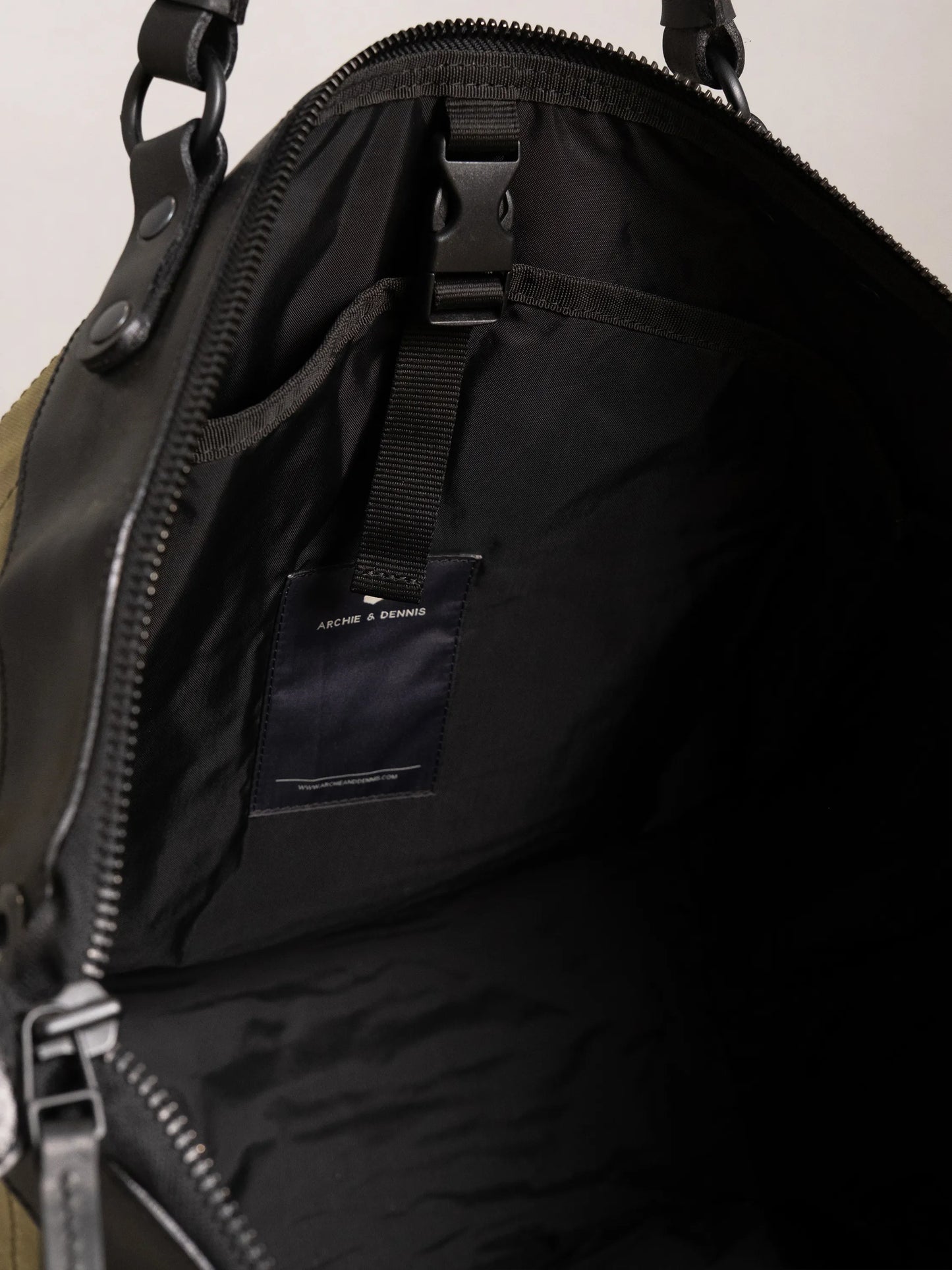 Interior view of a black-lined bag featuring zipped closure, an adjustable strap with buckle, and a small sewn label inside, highlighting artisanal construction details.