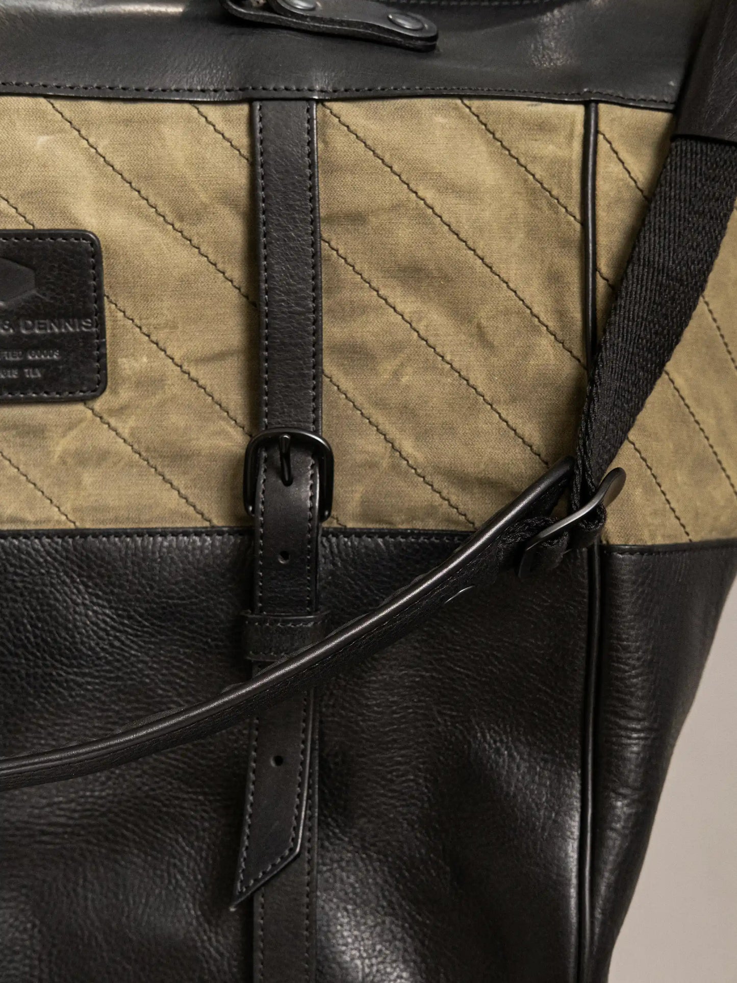 Close-up of an olive green and black handcrafted tote bag featuring quilted fabric, leather accents, adjustable strap, and detailed stitching.